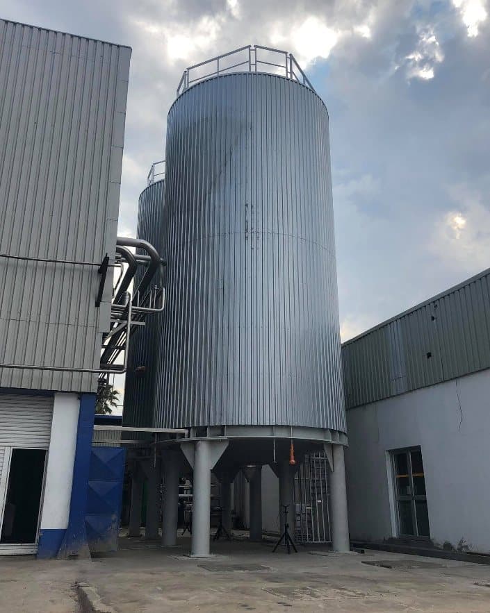 A tall storage silo alongside the plant building it serves
