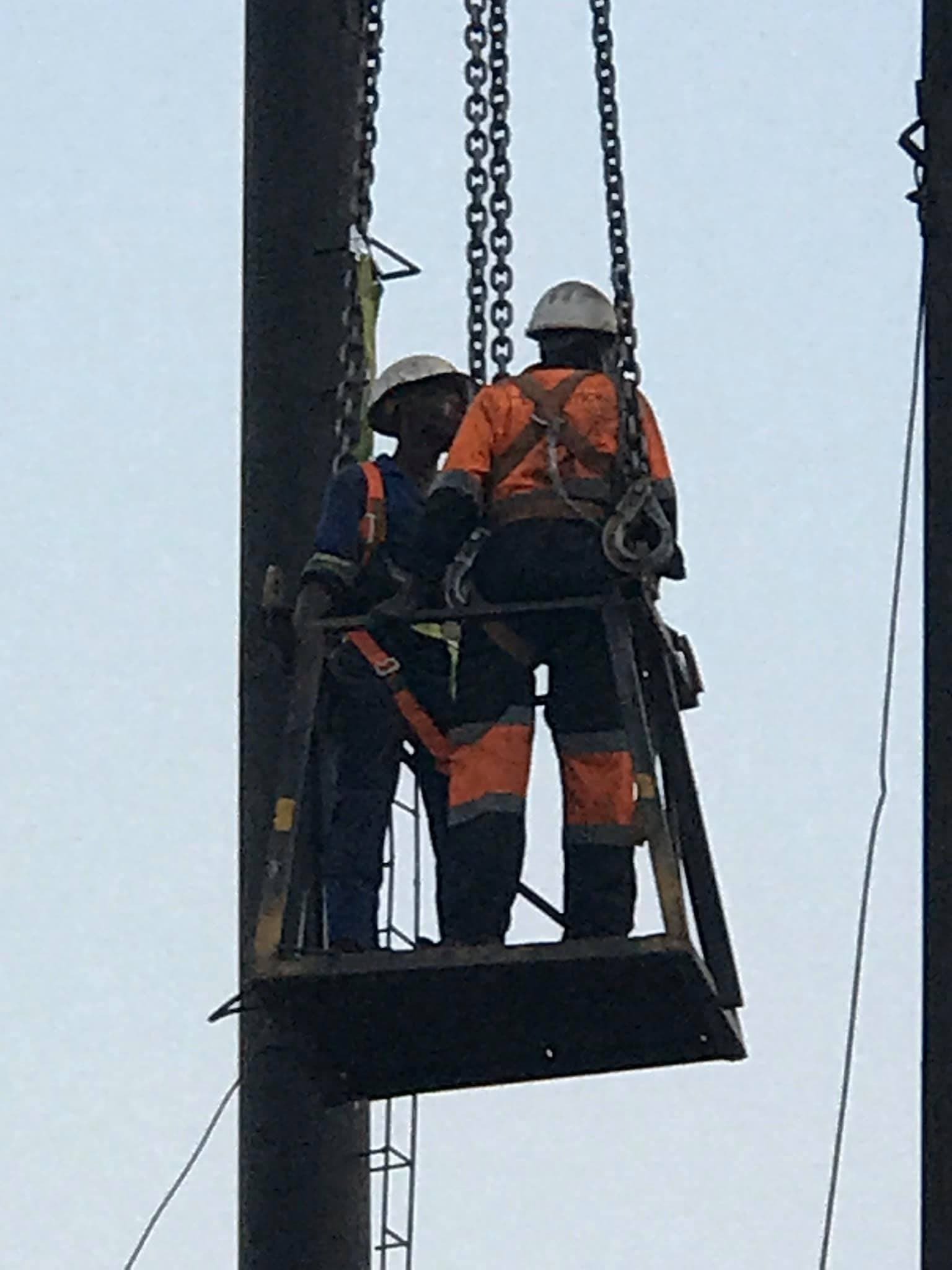 Two linesmen working from a suspended cradle on a mast