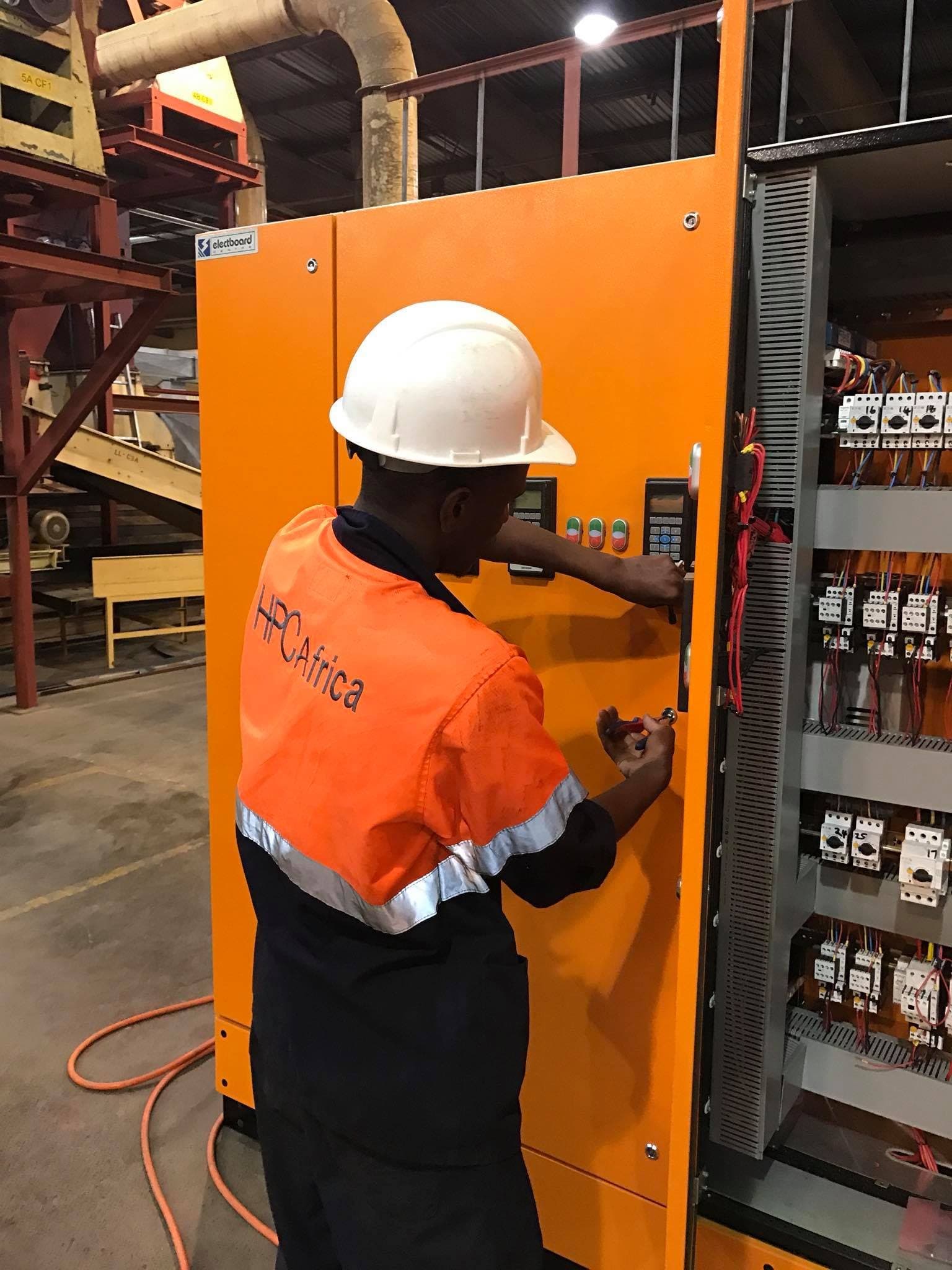 An electrician in HA GROUP branded PPE working at an open distribution panel