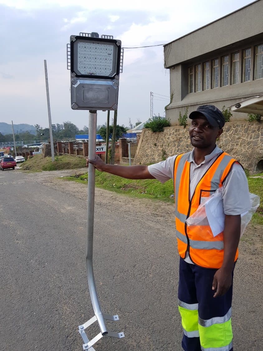 A technician holding a solar street-light luminaire before it is fitted